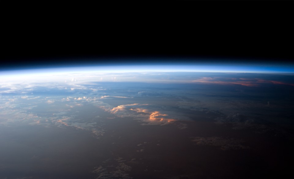 the blackness of outer space is seen above a thin haze of blue above the surface of the Earth